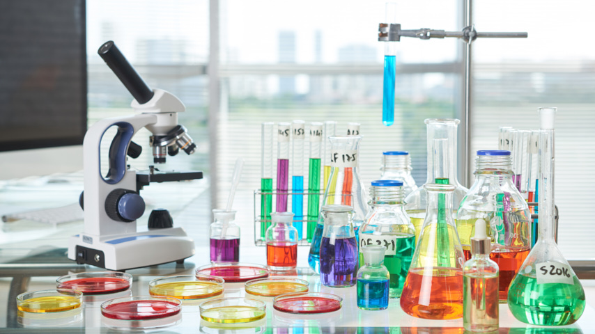 Sobre una mesa material de laboratorio, probetas, tubos de ensayo, microscopio, probetas